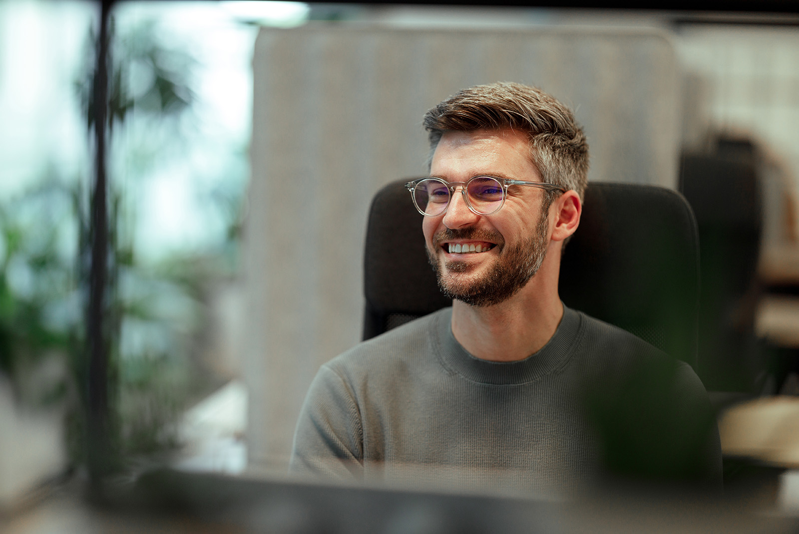 Mann sitzt an seinem Arbeitsplatz und lächelt in Beratungssituation